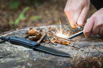 Men with knife using a magnesium fire steel to start a fire in the woods - obrazy, fototapety, plakaty