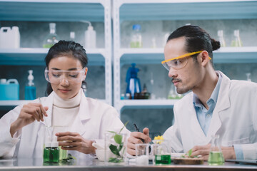 Researcher woman are mixing liquid in the beaker and researcher man are look to substance and notes on a pen to notebook in his hand at laboratory.