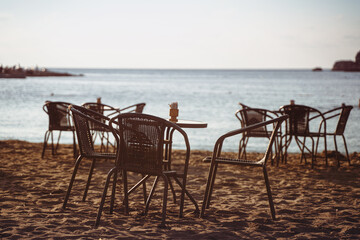 empty cafe table and chairs on sandy beach in front of sea golf with clear sky before sunset