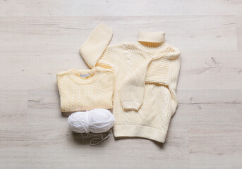 Children's knitted sweaters and ball of yarn on grey background