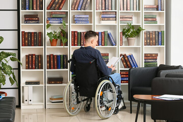 Young man in wheelchair choosing book in home library