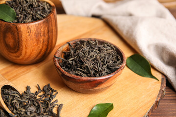 Bowls with dry tea leaves on wooden background