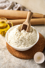 Bowl with flour and wooden scoop on table, closeup