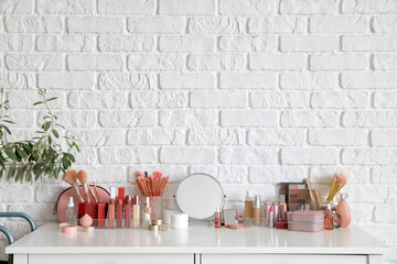 Organizer with makeup brushes, decorative cosmetics and mirror on table near white brick wall