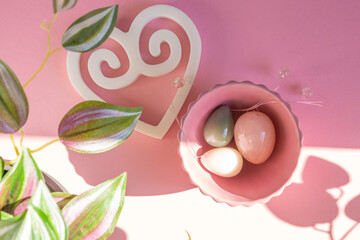 Colorful crystal yoni eggs laying in pink ceramic bowl on bright pink background