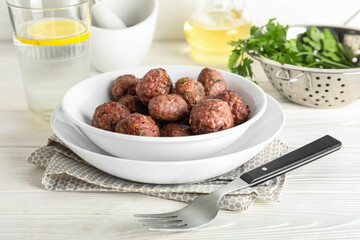 Plates with tasty meat balls and fork on white wooden background