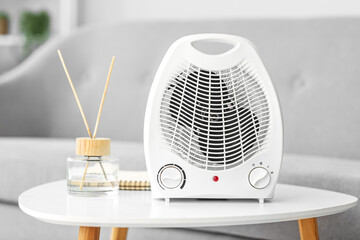 Electric fan heater, notebook and reed diffuser on table in living room