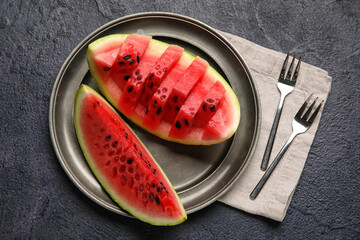 Plate with slices of watermelon, forks and napkin on dark background