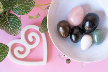 Colorful crystal yoni eggs laying in ceramic bowl on bright pink background