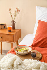 Wooden board with bowl of tasty granola and cup of coffee on bed