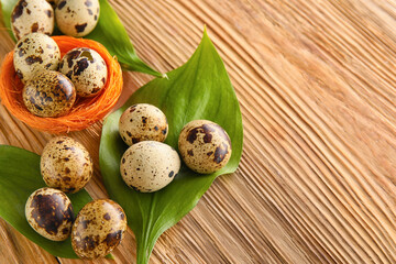 Fresh quail eggs and plant leaves on wooden table, closeup