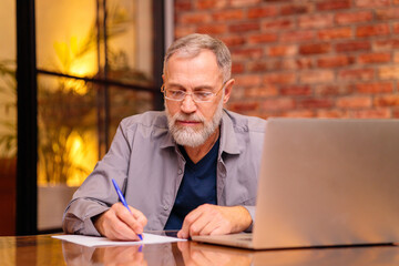 Smiling senior middle aged man in glasses working on laptop at home