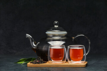 Wooden board with glass cups of black tea and teapot on dark background