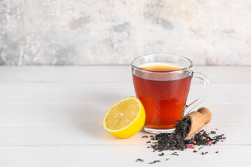 Cup of hot black tea and dry leaves on light background