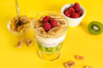 Glass of tasty chia seed pudding with fruits on yellow background