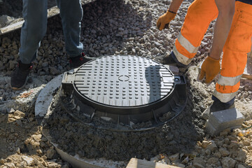 An cast iron sewer hatch in concrete base for installation of sewer well in ground is completed by installing - obrazy, fototapety, plakaty