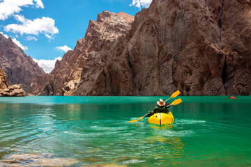 Kayaking on a mountain lake. Two men are sailing on a red canoe along the lake along the rocks. The theme of water sports and summer holidays.
