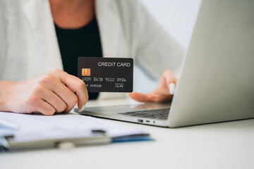 Woman holding a credit card and using a laptop computer to work online, shop online, and do banking online.