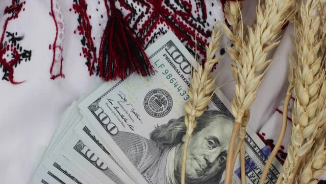 Spikelets of wheat on the background of dollars banknotes and national clothes. Blockade of the export of Ukrainian wheat. Famine in underdeveloped countries.