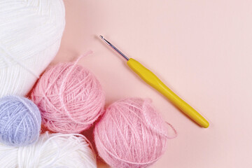 Threads for knitting in white, gray and pink colors on a pink background. Crochet hook and thread