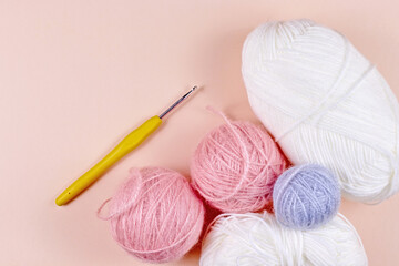 Threads for knitting in white, gray and pink colors on a pink background. Crochet hook and thread
