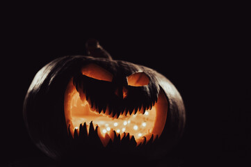 A creepy pumpkin with a carved grimace glows. Jack on a lantern in the dark.