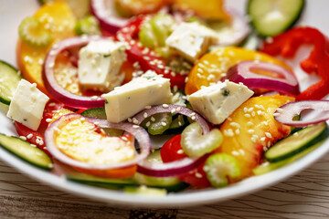 Various vegetables in a white plate: bell peppers, cucumbers, tomatoes, cheese, red onions, sesame seeds, celery, peaches.Vegetable salad with peaches.Vegan food and snacks. .