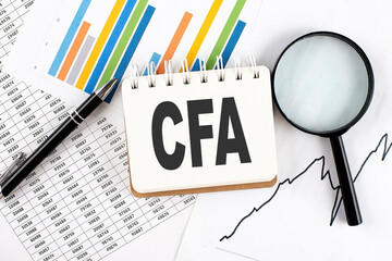 CFA - Chartered Financial Analyst text on notebook on the graph background with pen and magnifier