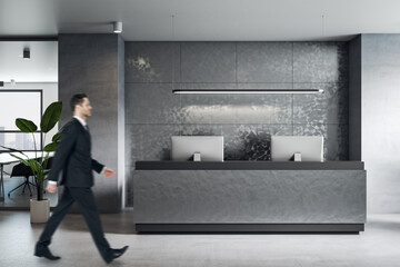 Side view on businessman walking by stylish dark furniture reception area in grey shades office