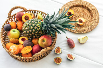 Pineapple and other exotic fruits in a wicker basket on a white background.