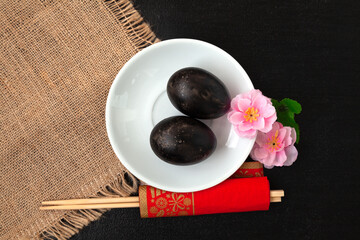 Black eggs, sakura flowers and chopsticks on a dark background