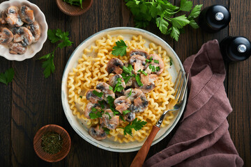 Fusilli pasta with mushrooms, cheese and garlic creamy sauce on plate on old wooden dark table background. Top view. Traditional Italian cuisine.