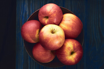 Top view of ripe red apples in earthenware bowl on a dark blue background
