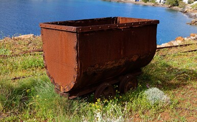 Old rusty coal tub or trolley on tracks, on the sea cliff in Megalo Livadi village, Serifos island, Greece