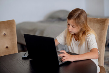 A cute little girl using her laptop to do a online lesson at home