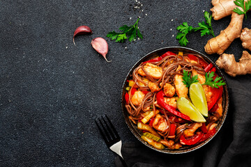 Asian cuisine, stir fry noodles with chicken and vegetables and sesame seeds in bowl. Black kitchen table background, top view, copy space