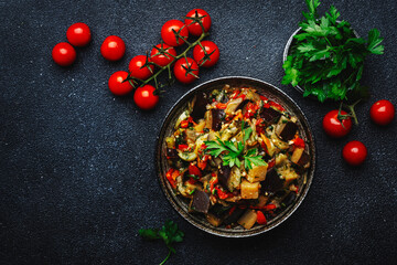 Vegetable stew, saute or caponata. Stewed eggplant with paprika, tomatoes, herbs and spices. Black kitchen table background, top view, copy space