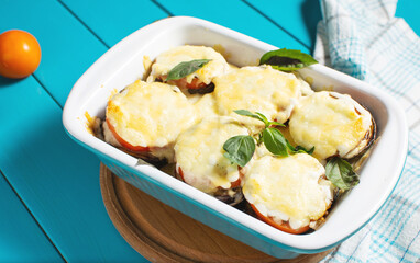 Eggplant baked with mozzarella cheese, tomatoes in baking dish on blue wooden table. Vegetarian food recipe