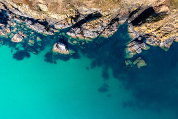 Aerial view directly above rugged coastal cliff jutting into calm turquoise ocean