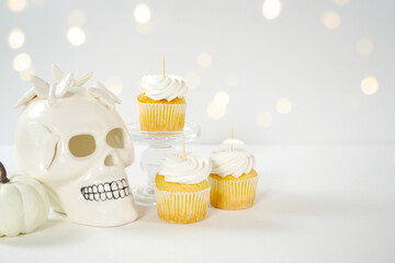 Halloween product mockup. Party treats cupcakes with white skull pumpkins against a white background with bokeh party lights. Negative copy space.