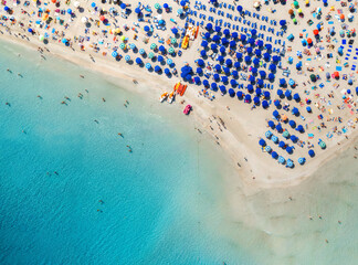 Top view of beautiful sandy popular beach La Pelosa with turquoise sea water and colorful umbrellas, Islands of Sardinia in Italy, aerial drone shot