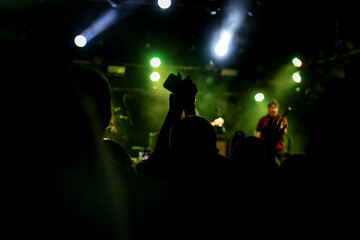 Fototapeta na wymiar Foco em mão de pessoa segurando uma taça no meio do público em um show com luzes coloridas.