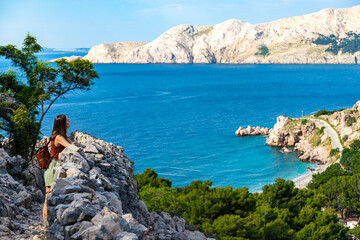 beautiful girl walks on the rocks on the shore of the adriatic enjoying the wonderful views in the background; vacation in croatia on krk island; hiking by vrzenica beach trail