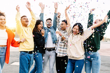 Group of diverse young friends celebrating together enjoying party throwing confetti outdoors -...