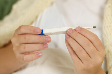 A teenage girl holds a thermometer with both hands. Close-up.