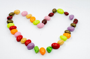 Heart made of colorful candy dragees. Dragee candies isolated on white background. Heart figure made of candy.
