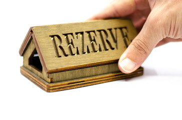 Table reservation letter. Human hand holding reservation sign. Wooden reservation drawn from the back on an isolated white background.
