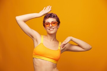 Young woman in a bright yellow fitness tracksuit with an open belly and sunglasses on an orange...
