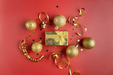 Christmas decorations for the New Year. Festive red background with golden sparkling baubles, streamers, confetti and gift box.