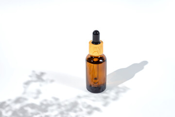 Amber dropper bottle with serum or gel on white background with daylight with beautiful flowers shadows. Skincare natural cosmetic.